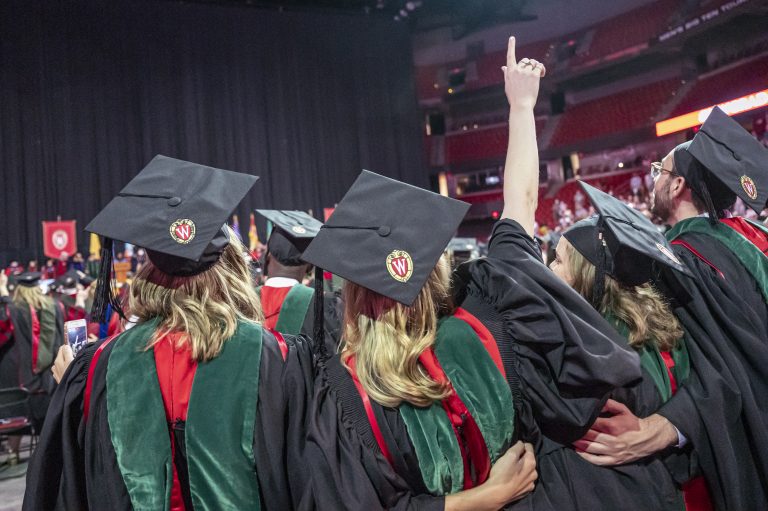 Small group of graduates standing side-by-side looking onstage.