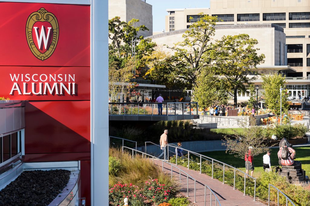 Side of building with text that reads, Wisconsin Alumni, and a UW–Madison crest next to Alumni Park.