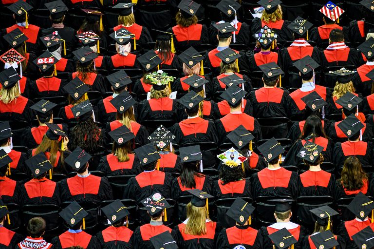 View from above of showing group of graduates seated wearing red and black academic attire.