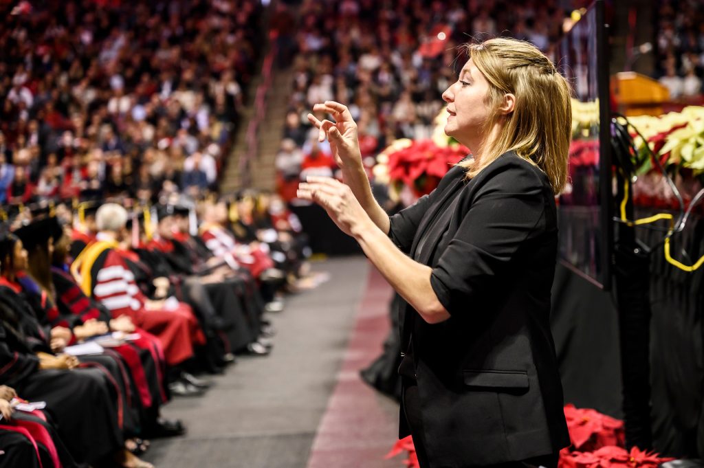 Sign language interpreter signs spoken comments during commencement ceremony.