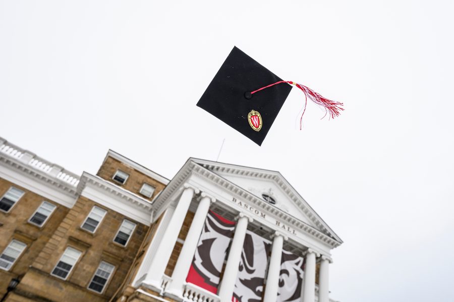 Graduation mortarboard and cap tassel tossed in sky in front of Bascom Hall.