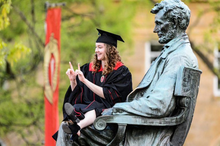Student wearing graduation attire siting on Abraham Lincoln statue.