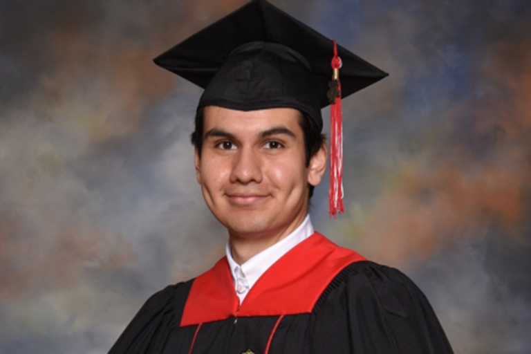 Portrait of a UW Madison graduate in front of a grey background wearing a cap and gown