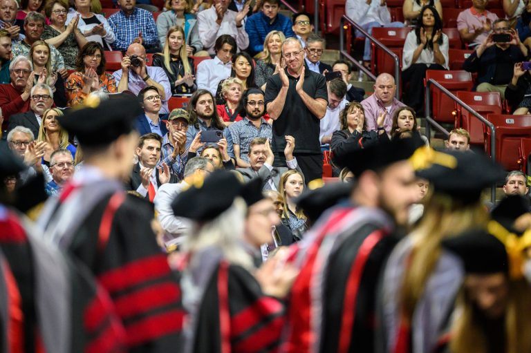 Family members clapping in background overlooking graduate candidates.