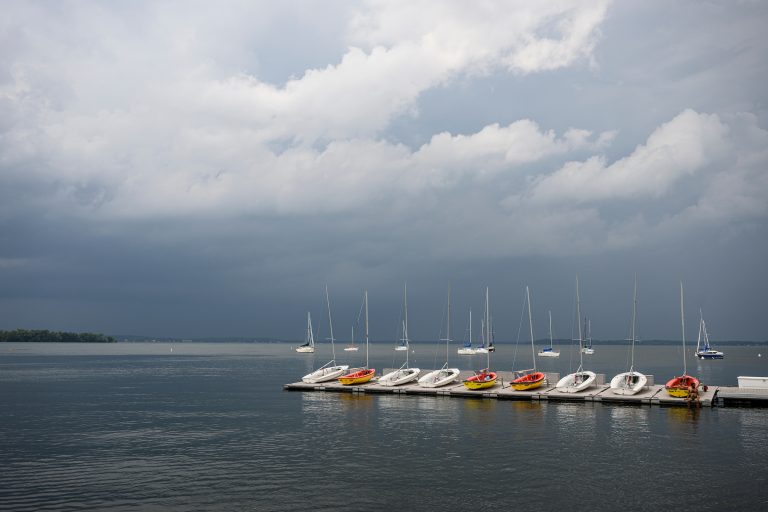 Storm clouds rolling in distance over row of docked boats on lake.