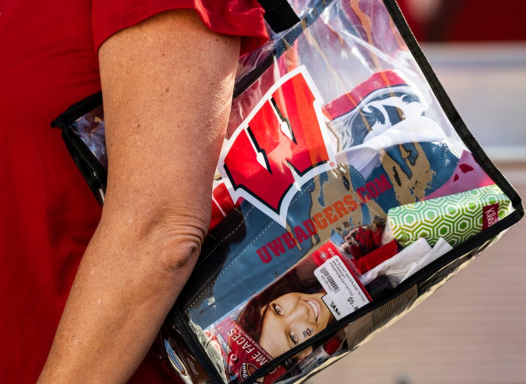 Person carries clear plastic shoulder bag branded with Motion W filled with items.