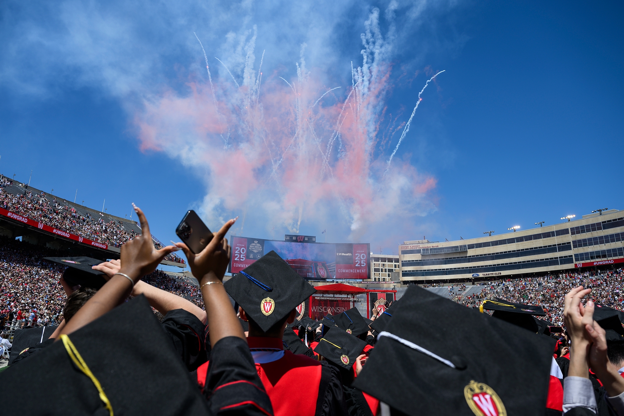 A person raises their hands to make a W as the crowd looks ahead at a fireworks display.