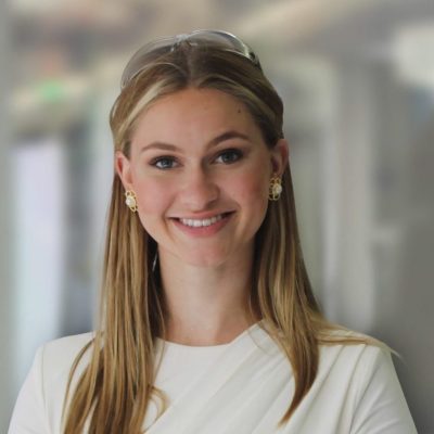 Headshot of Grace Stanke, wearing a white shirt standing in front of a window