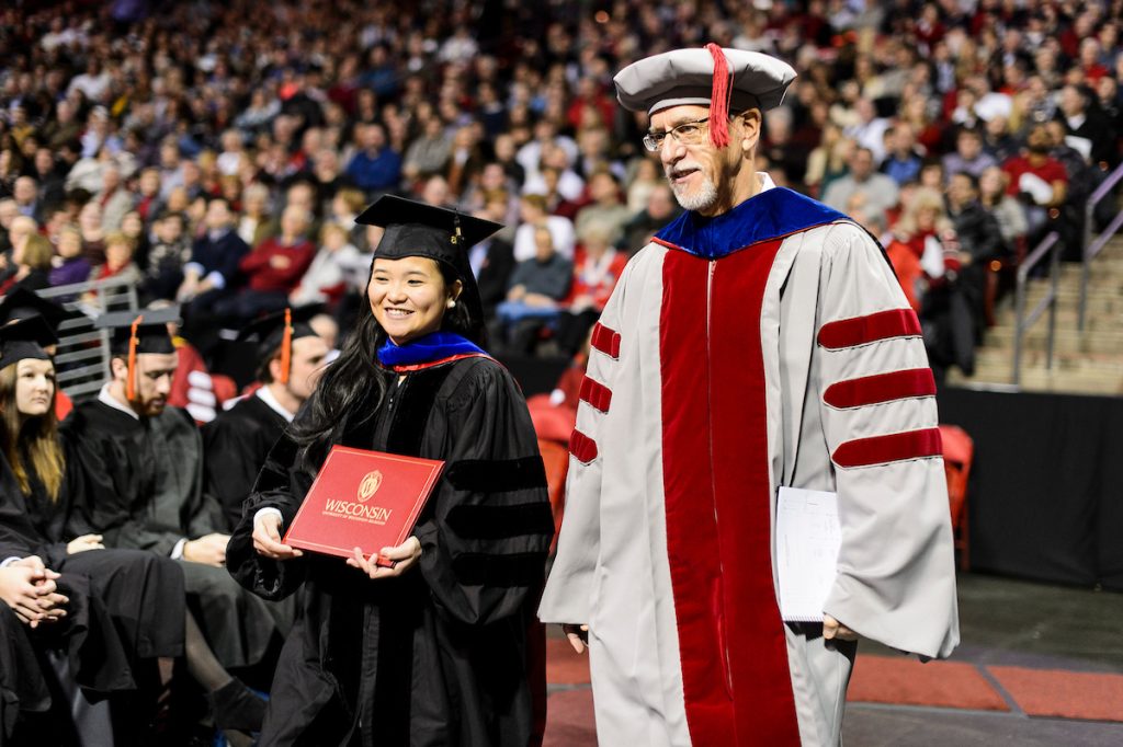 Faculty member in academic attire walking alongside a graduate candidate.