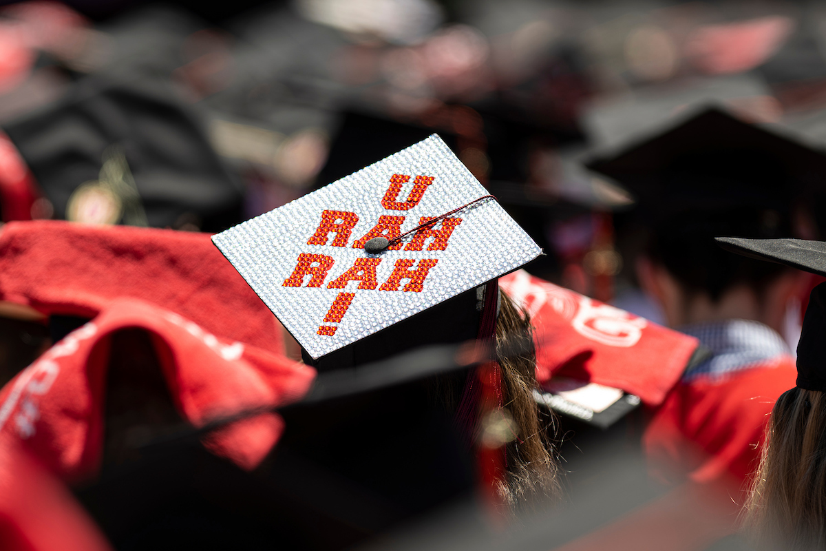 In a crowd of soon-to-be graduates, the top of a student's cap stands out with "U Rah Rah" spelled out in sequins