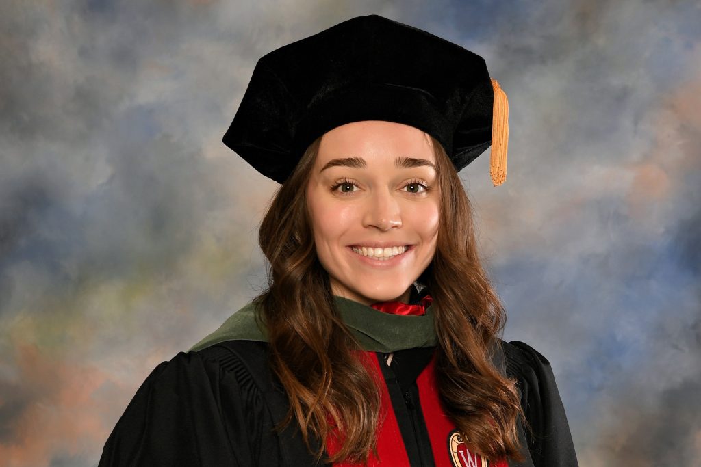 UW–Madison graduate poses in cap and gown for a studio portrait session.